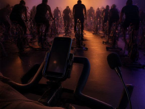 An instructor's bike console with a phone mounted, riders beyond.