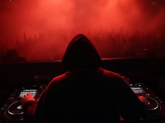 A DJ from behind in a red-lit booth, phone on the booth edge.